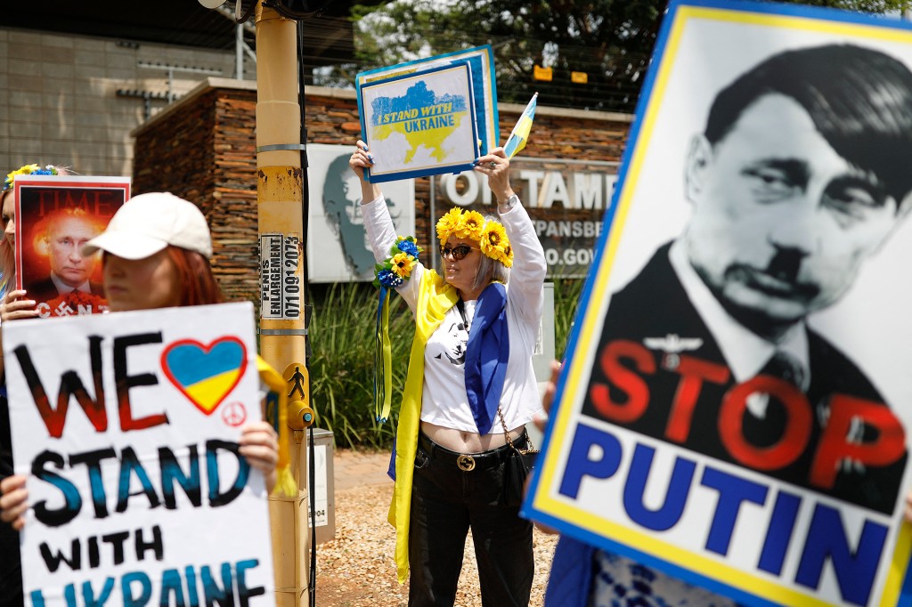 南アフリカウクライナ協会の支持者は、ウクライナを支持して抗議するプレトリアを通過する運転手に反戦ポスターを振る。