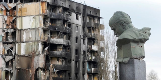 2022年4月6日水曜日、ウクライナのボロディンカの中央広場でロシアの爆撃で破壊された集合住宅を背景に、ウクライナの詩人タラスシェフチェンコの記念碑と国家のシンボルが、弾丸の痕跡とともに現れます。 