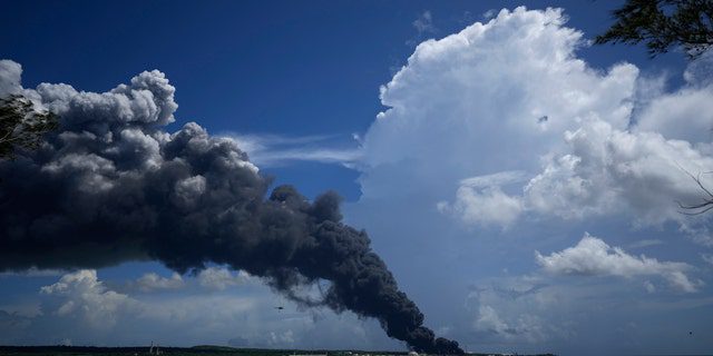 2022 年 8 月 6 日土曜日、キューバのマタザナスで、前夜の雷雨の際に発生した火災を消防士が消火しようとしているときに、巨大な煙の柱がスーパータンカー マタンザスの基部から立ち上っています。