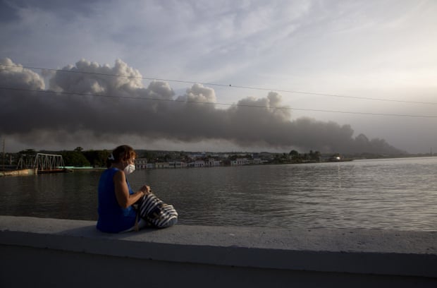 マレコンの防波堤に座る住人。背景には火災の煙が立ち上っている。