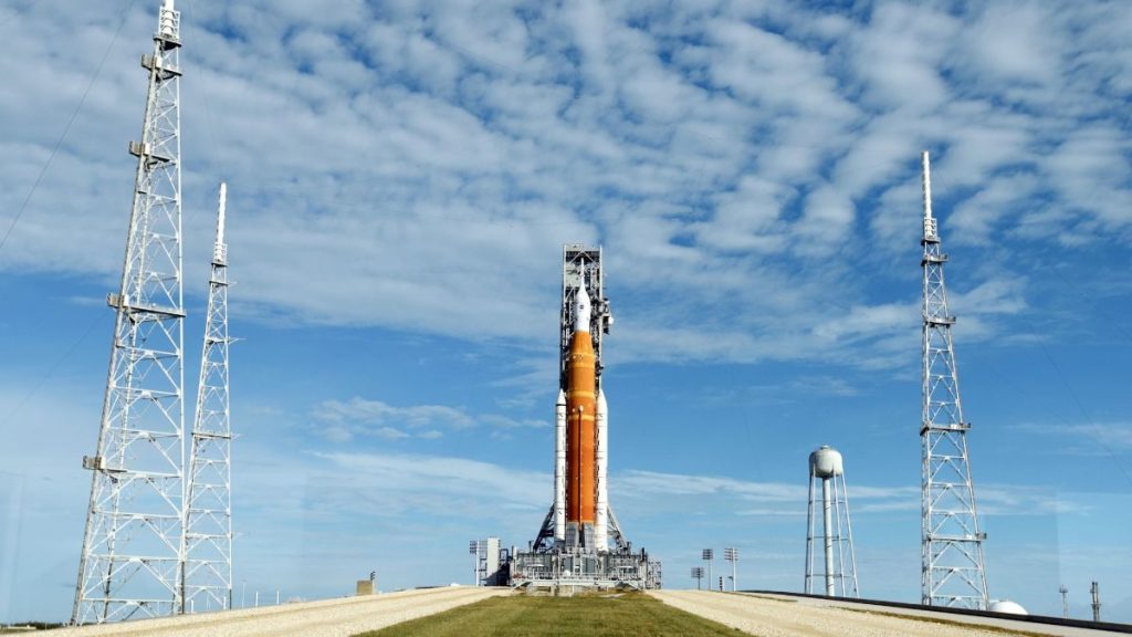 The Artemis 1 moon rocket stands tall on the launch pad with blue sky and clouds above.