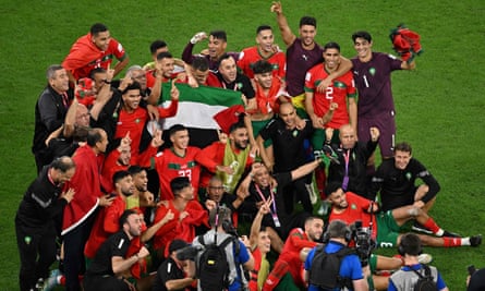 赤いシャツを着た選手たちがピッチ上で写真を撮り、祝賀のジェスチャーをしている。 グループの真ん中でパレスチナの旗を掲げる数人の選手